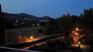 A nighttime view of a landscaped area with pathways, trees, and distant city lights. - Studio with balcony, sea & golf view, swimming pool, parking-Hameau Cap Esterel (Saint-Raphaël)