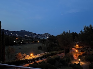 A nighttime view of a landscaped area with pathways, trees, and distant city lights. - Studio with balcony, sea & golf view, swimming pool, parking-Hameau Cap Esterel (Saint-Raphaël)