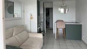 A modern living space with a sofa, a stool, a kitchen area, and a mirror. - Studio with balcony, sea & golf view, swimming pool, parking-Hameau Cap Esterel (Saint-Raphaël)