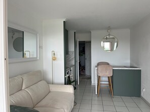A modern living space with a sofa, a stool, a kitchen area, and a mirror. - Studio with balcony, sea & golf view, swimming pool, parking-Hameau Cap Esterel (Saint-Raphaël)