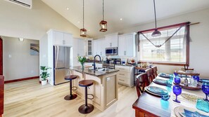 Una cocina moderna con armarios blancos, electrodomésticos de acero inoxidable y una isla central con taburetes.