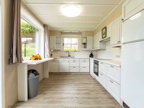 A kitchen with white cabinetry, a window with curtains, a trash bin, and a wooden floor. - Villa Esterel with garden & parking by Interhome (De Haan)
