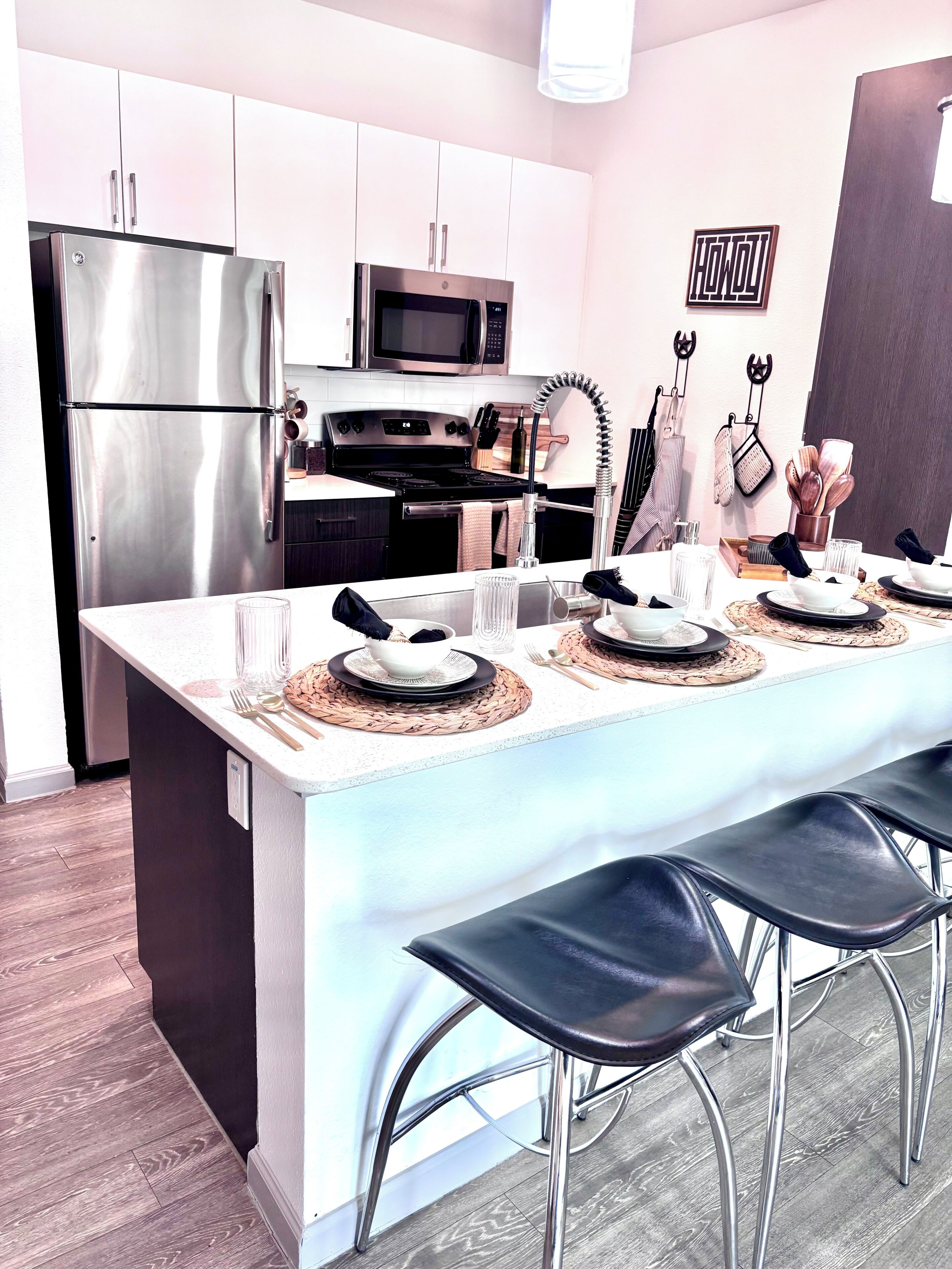 Une cuisine moderne équipée d’appareils électroménagers en acier inoxydable, un coin repas avec une longue table et des tabourets, et un four à micro-ondes fixé au mur.