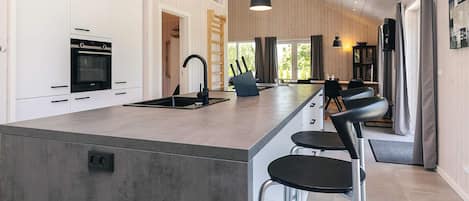 Ett modernt kök med en central köksö, rostfria vitvaror och barstolar.