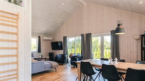 En rummelig opholdsstue med trægulv, et spisebord med stole, en sofa og et fjernsyn ophængt på væggen.