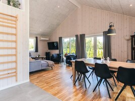 En rummelig opholdsstue med trægulv, et spisebord med stole, en sofa og et fjernsyn ophængt på væggen.