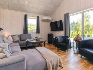 A modern living room with a sofa, armchairs, a coffee table, and a flat-screen TV mounted on the wall. - 5 Star Holiday Home in Vaeggerlose (Vaeggerlose)