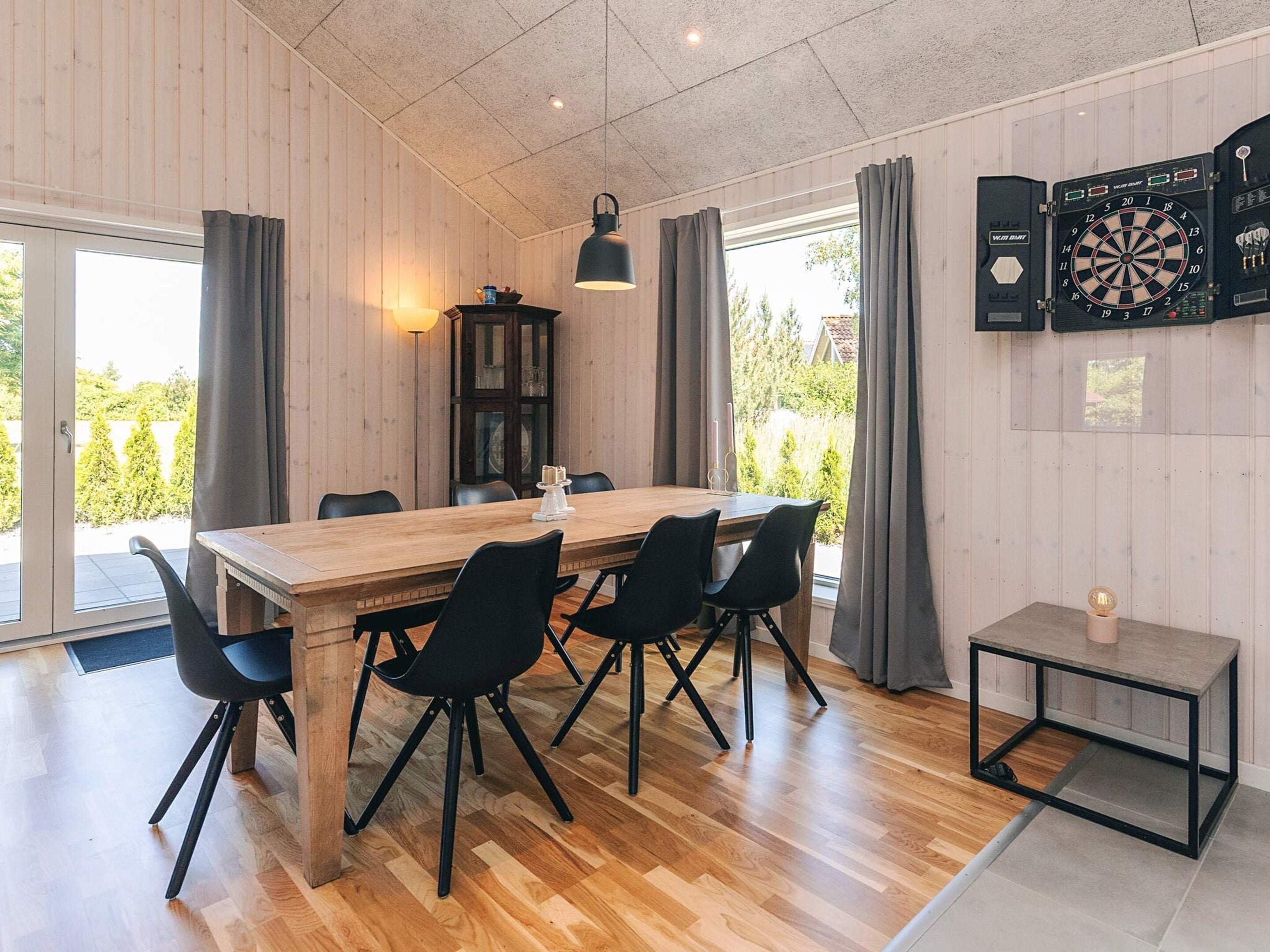 A dining area with a wooden table, black chairs, a cabinet, and a dartboard.