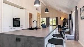 Et moderne køkken med en central ø, rustfrie hårde hvidevarer og barstole.