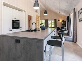 Et moderne køkken med en central ø, rustfrie hårde hvidevarer og barstole.