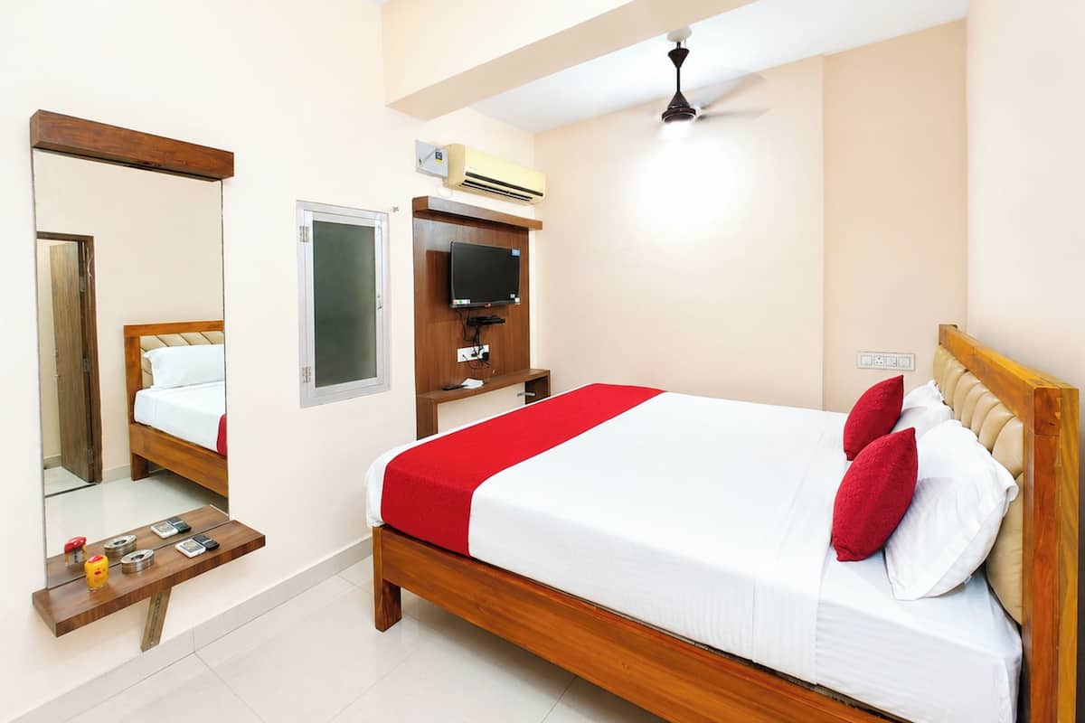 Una habitación de hotel con cama, televisión, aire acondicionado, ventilador de techo, espejo y mesita de noche.