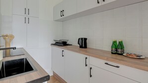 A modern kitchen with white cabinets, a wooden countertop, a sink, and two green bottles. - Kraszewskiego 21 by Grand Apartments (Sopot)