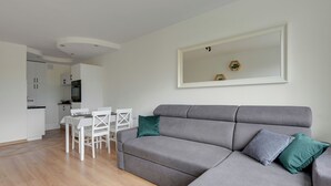 A modern living room with a grey sofa, a dining table, and chairs. There is a kitchen in the background. - Kraszewskiego 21 by Grand Apartments (Sopot)