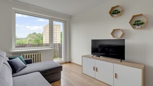 A modern living room with a sofa, TV, and hexagonal wooden shelves with plants. - Kraszewskiego 21 by Grand Apartments (Sopot)