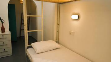 A single bed with a white pillow, a wooden ladder, a white dresser, and a green door in a room with a white wall and a light fixture.