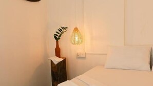 A neatly made bed with white linens, a bedside table with a vase and a lamp, and a wooden bench at the foot of the bed. - Fins Arugambay (Arugam Bay)