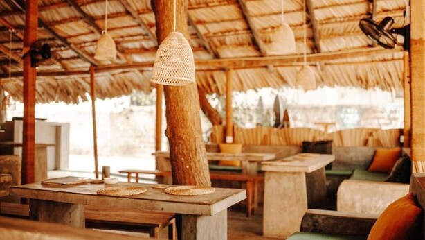 A rustic outdoor seating area with wooden tables and benches, a thatched roof, and hanging light fixtures. - Fins Arugambay (Arugam Bay)