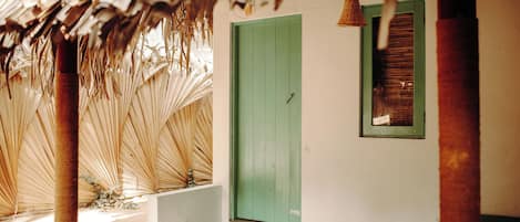 A building with a green door, a window with shutters, and a thatched roof structure.