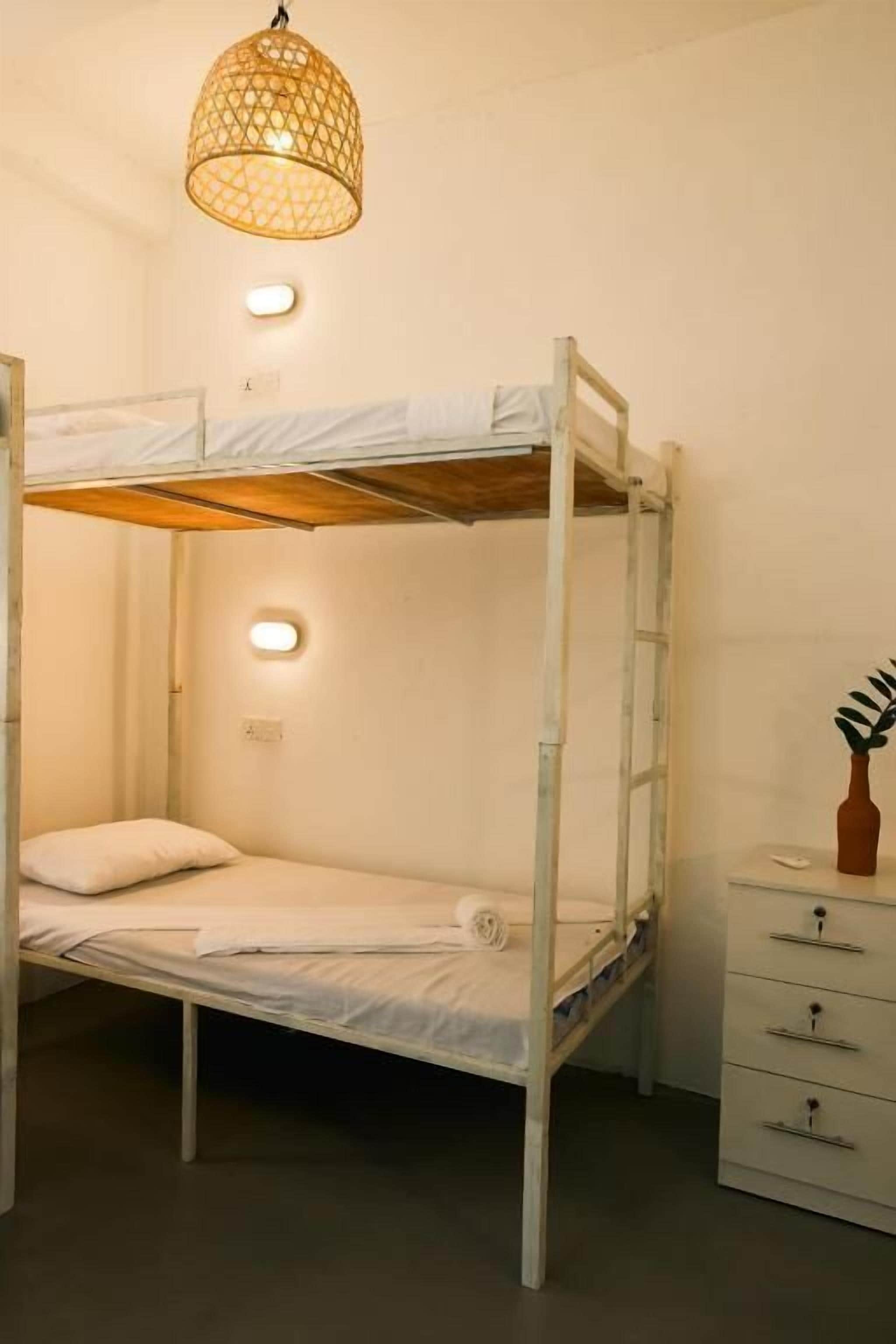 A bunk bed with a ladder, a bedside table with drawers, and a hanging light fixture.