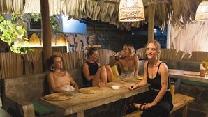 A group of people seated at a wooden table with woven placemats, under thatched roof and woven light fixtures. - Fins Arugambay (Arugam Bay)