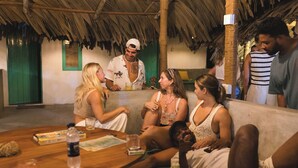 A group of people sitting on a wooden table and a couch in a room with a thatched roof and green walls. - Fins Arugambay (Arugam Bay)