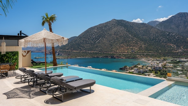 Una piscina con sillas de descanso y una palmera, con vistas a un paisaje montañoso y una extensión de agua.