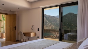 Un dormitorio con una cama grande, un escritorio, una silla y vistas a montañas a través de un ventanal.