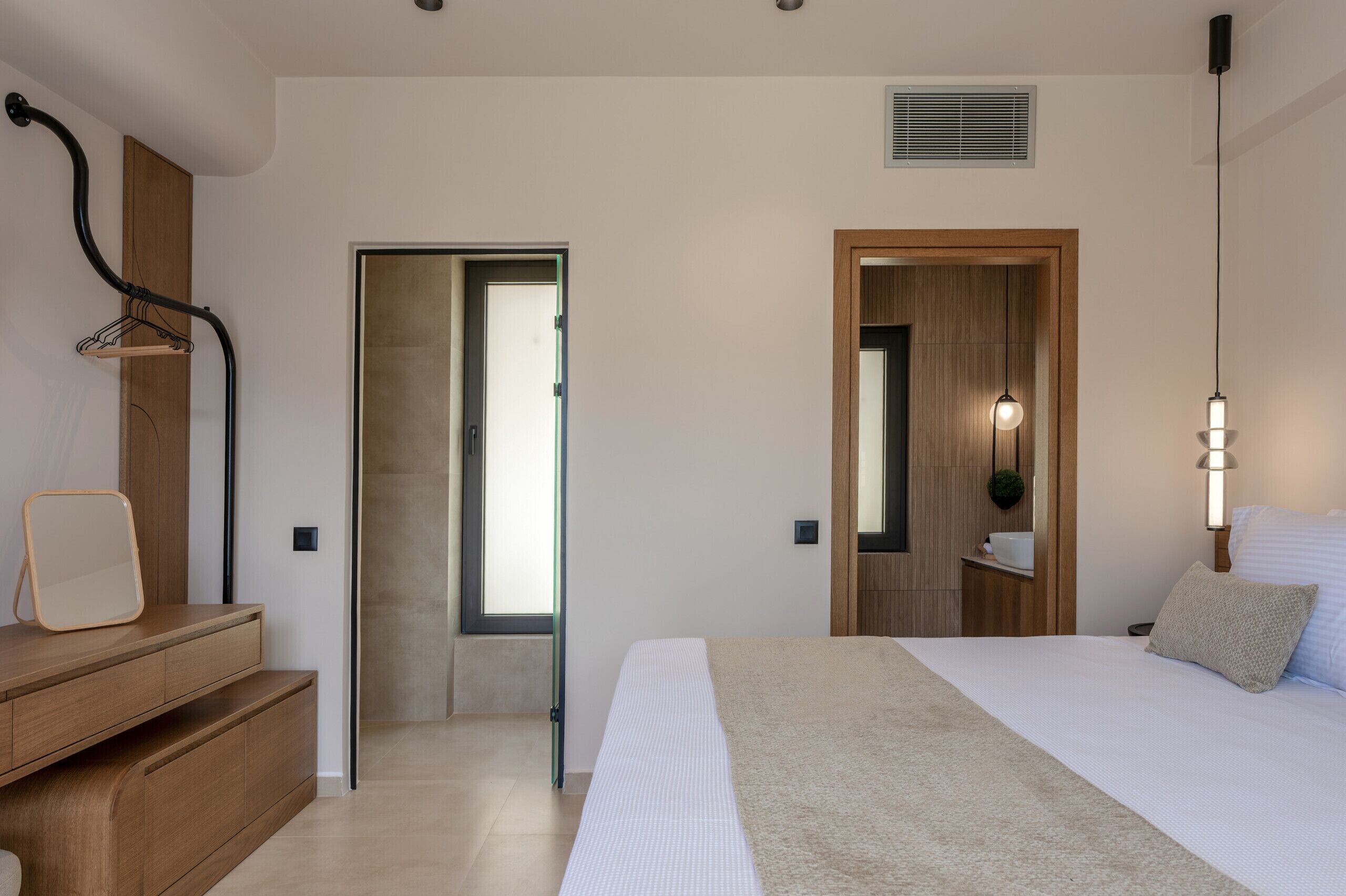Un dormitorio con cama, mesita de noche, lámpara y una puerta que da a otra habitación.