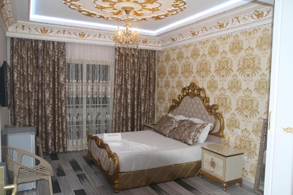 A bedroom with a bed, curtains, a chandelier, a bedside table, and a chair.