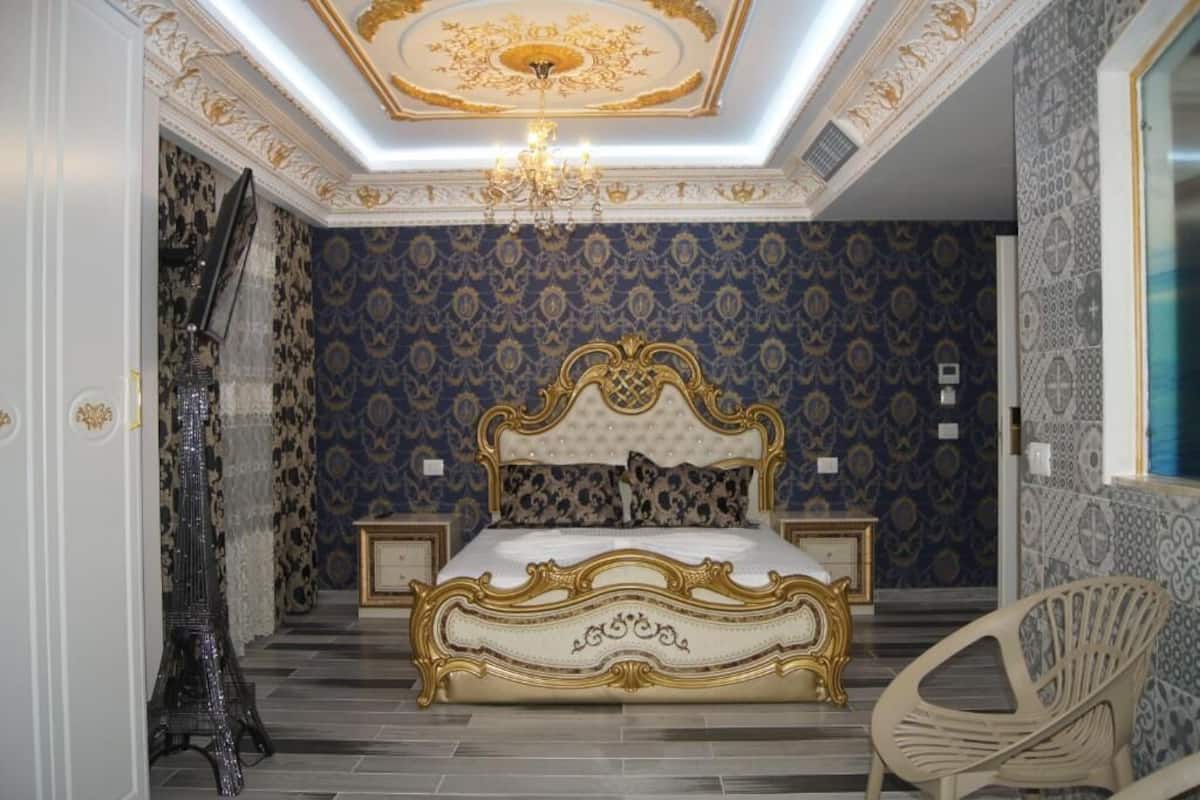 Un dormitorio con una cama grande y ornamentada, un candelabro, papel tapiz estampado y una silla.