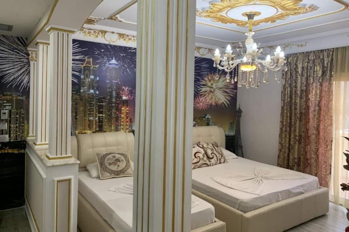Un dormitorio con un mural de paisaje urbano, una araña y una cama con almohadas decorativas.