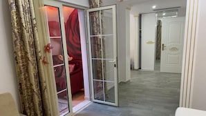A hallway with a sliding glass door leading to a room with a red carpet and a white door with gold accents. - Hotel Antalya Beach Durres (Durrës)