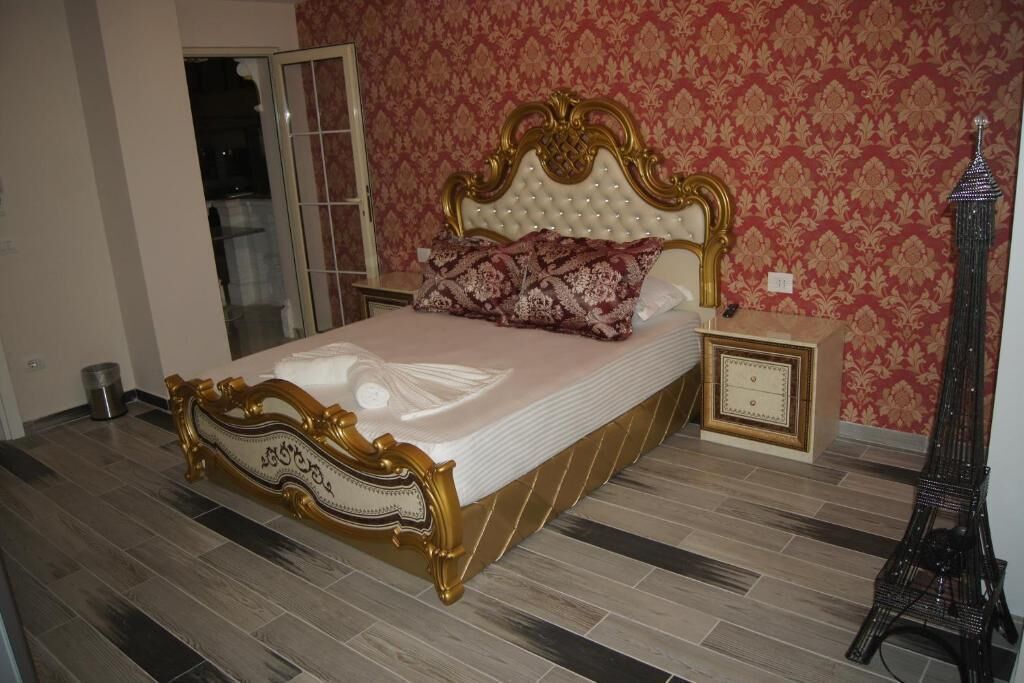 A bed with ornate headboard, a nightstand, a wall clock, and a decorative Eiffel Tower.