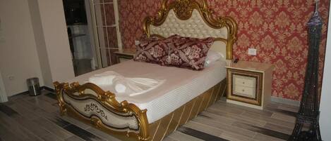 A bed with ornate headboard, a nightstand, a wall clock, and a decorative Eiffel Tower.