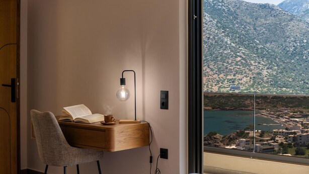 A modern room with a desk, chair, and a view of a coastal town and mountains. - Azur Blue Luxury Villa (Mylopotamos)