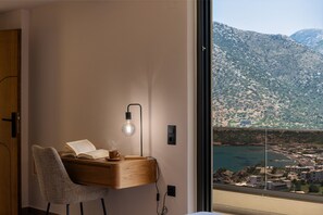 A modern room with a desk, chair, and a view of a coastal town and mountains. - Azur Blue Luxury Villa (Mylopotamos)