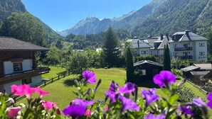 A mountain landscape with a hotel featuring multiple buildings, a wooden house, and a well-maintained lawn. - Pension Monika (Kaprun)