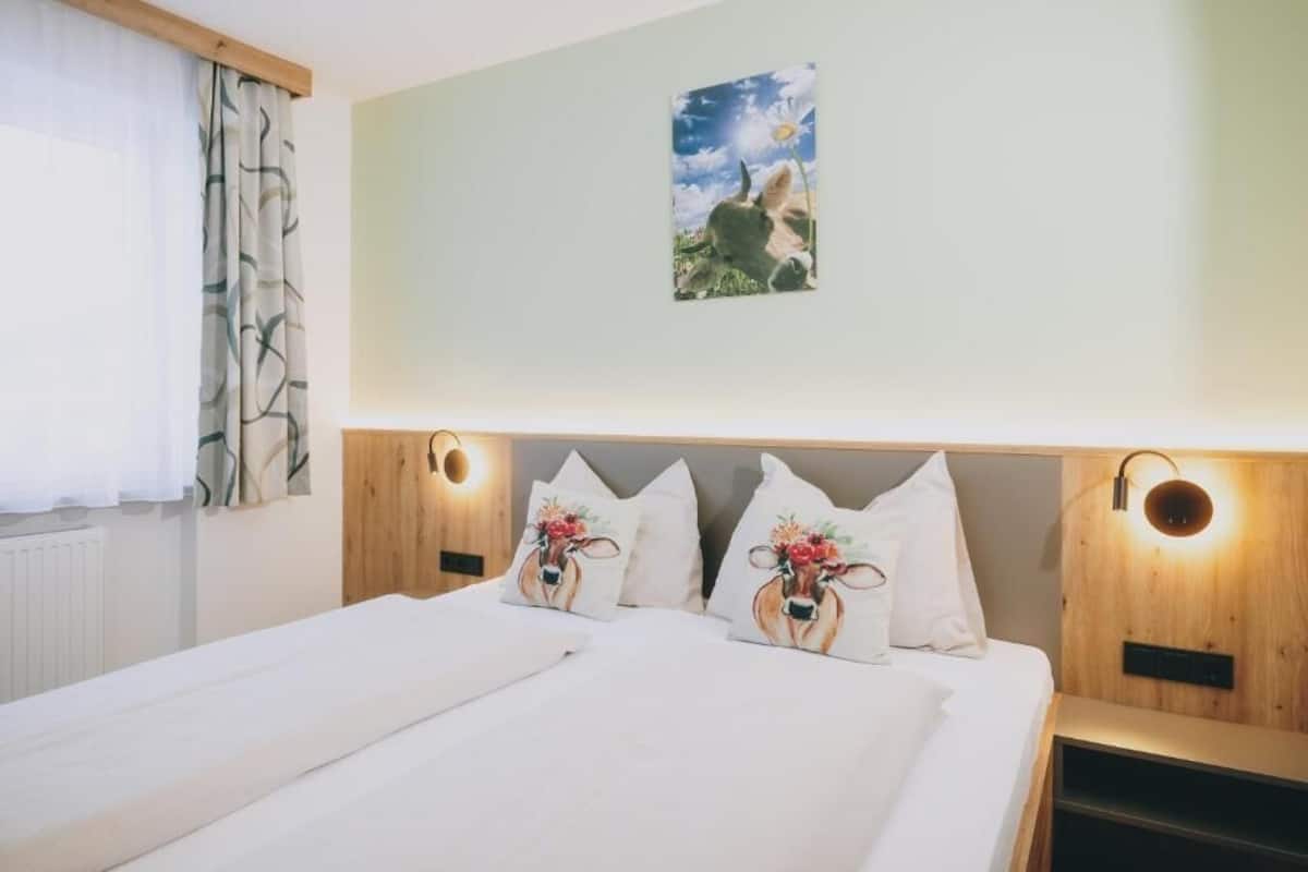 A hotel room with a bed, two wall-mounted lamps, a painting, and a window with curtains.