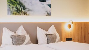A neatly made bed with white and gray pillows, a wooden headboard, a wall-mounted light fixture, and a framed picture above the bed. - Pension Monika (Kaprun)