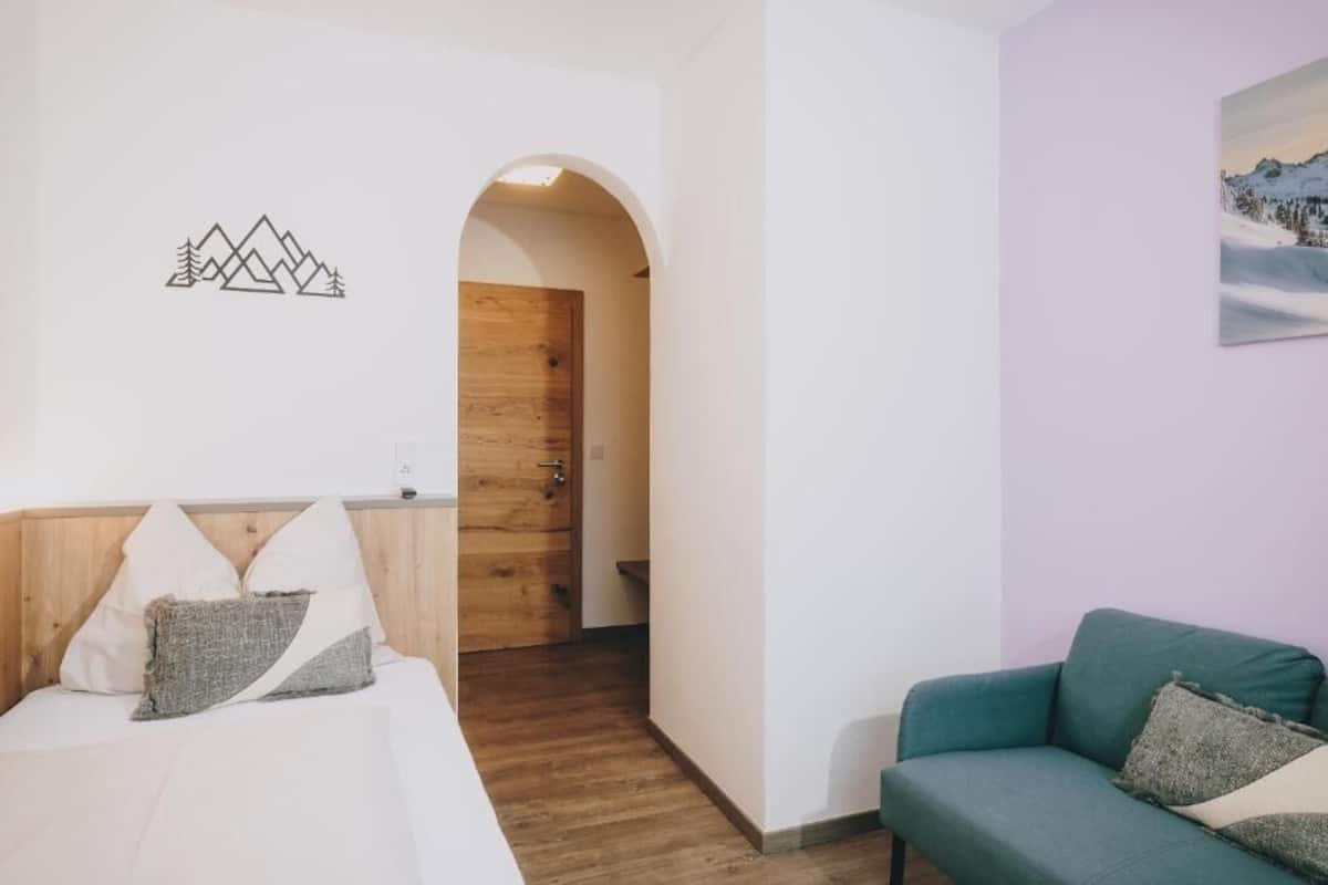 A room with a wooden door, a green sofa, and a white bed with pillows.