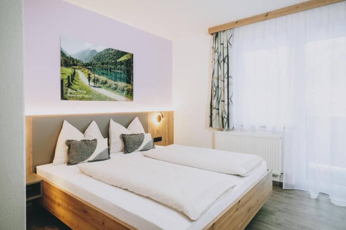 A double bed with a wooden headboard, a night light, and a landscape painting on the wall.
