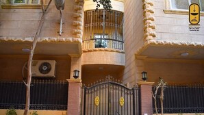 Un immeuble à plusieurs étages doté d’une entrée sécurisée par un portail, de balcons et d’un logo représentant « Nb.Nir Pyramids Inn ».