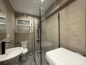 Een badkamer met een toilet, een wastafel, een douchecabine van glas en een spiegel.
