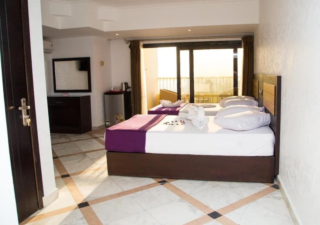 A hotel room with a bed, a desk, a chair, a mirror, and a window with a view.