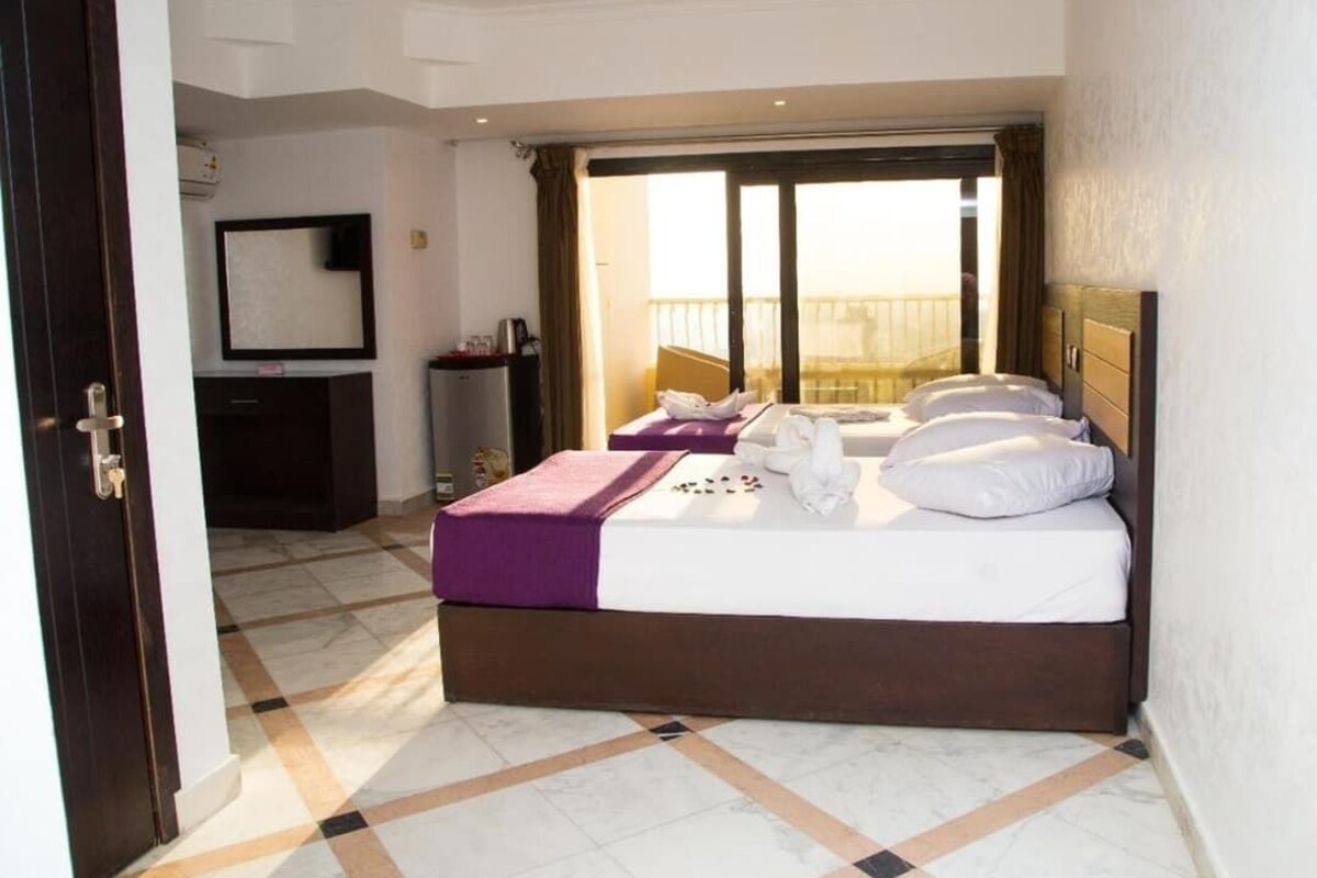 A hotel room with a bed, a desk, a chair, a mirror, and a window with a view.