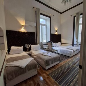 Een hotelkamer met twee bedden, een stoel, een klein tafeltje met een bloevas en een raam met gordijnen.
