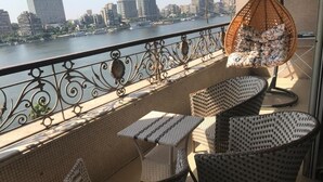 Un balcon agrémenté de meubles en osier, d’un fauteuil suspendu et offrant une vue sur les toits d’une ville, de l’autre côté d’une rivière.