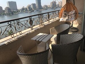 A balcony with wicker furniture, a hanging chair, and a view of a city skyline across a river. - Basuiony hotel  (Giza)