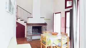 A dining area with a fireplace, wooden chairs, and a table with a bowl. - Les Gites du Bois de Chelles (La Chapelle-Geneste)