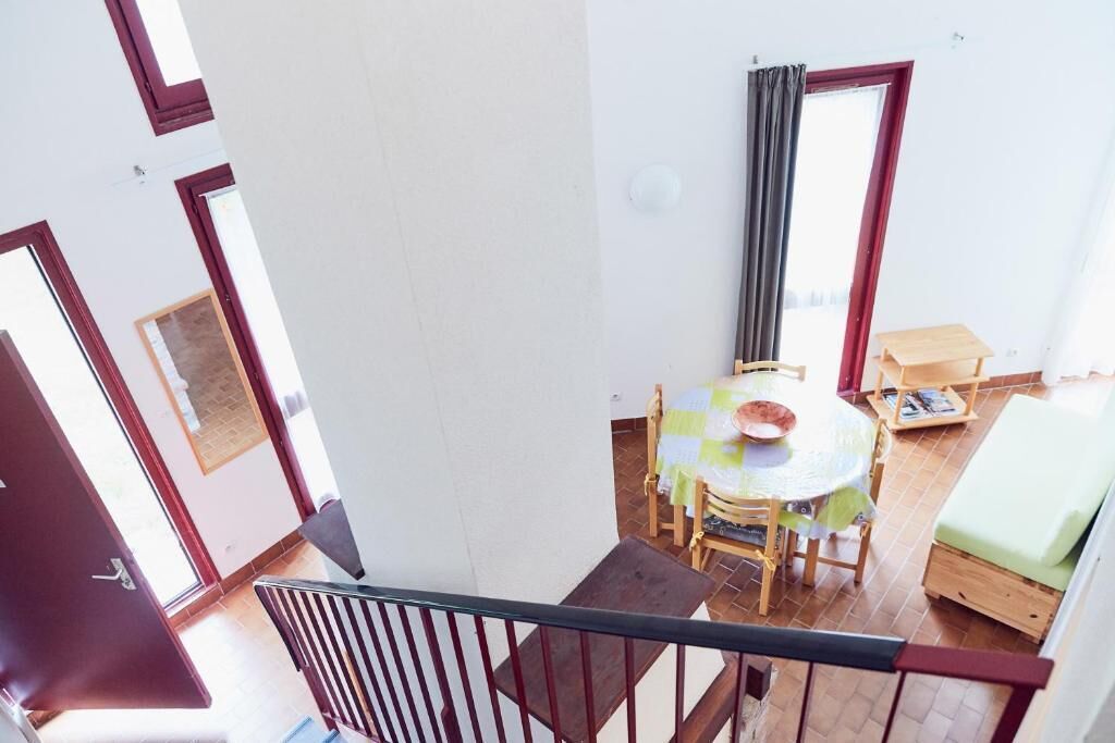 Et værelse med spisebord, stole, en lille sofa, et vindue med gardiner og en trappe.